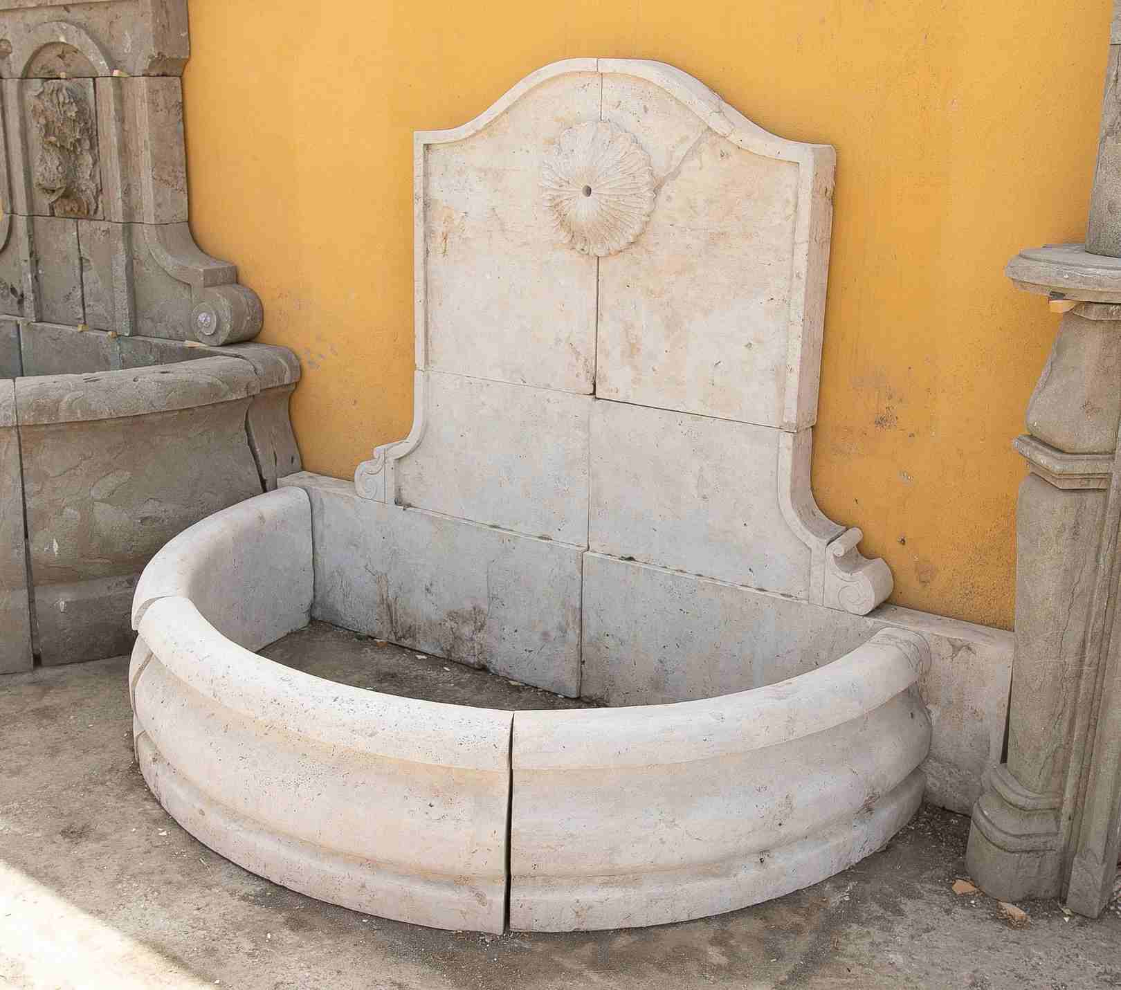 Fuente de pared de mármol tallado con una pileta semicircular y una roseta clásica.