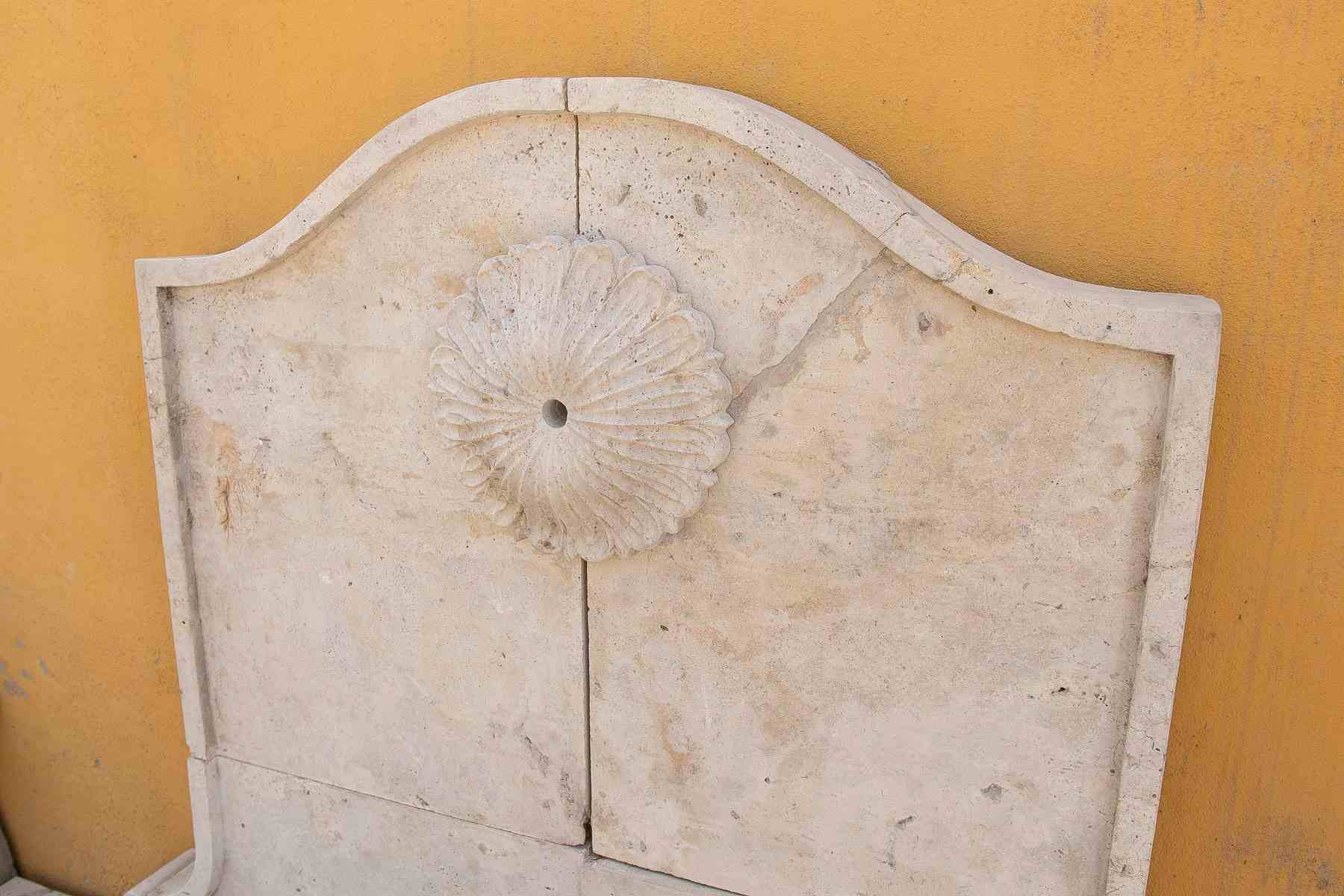 Fuente de pared de mármol tallado con una pileta semicircular y una roseta clásica.