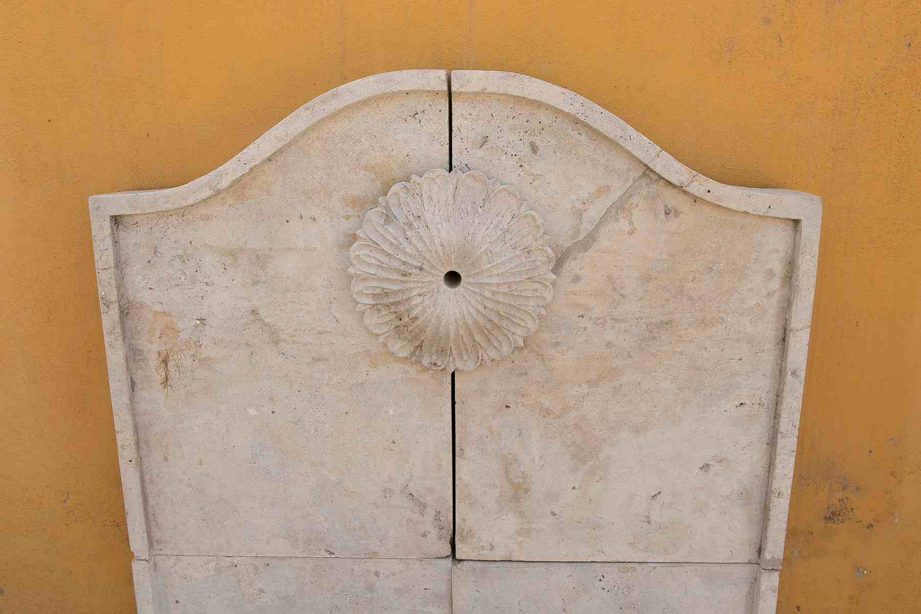 Fuente de pared de mármol tallado con una pileta semicircular y una roseta clásica.